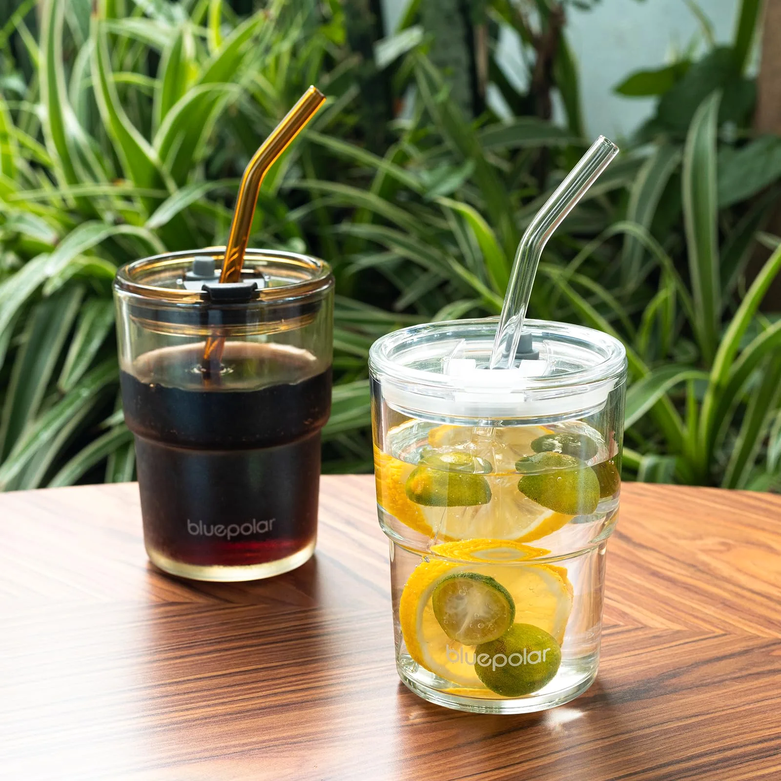 Two clear 13 oz glasses on a wooden table, one with iced coffee and one with lemon water.
