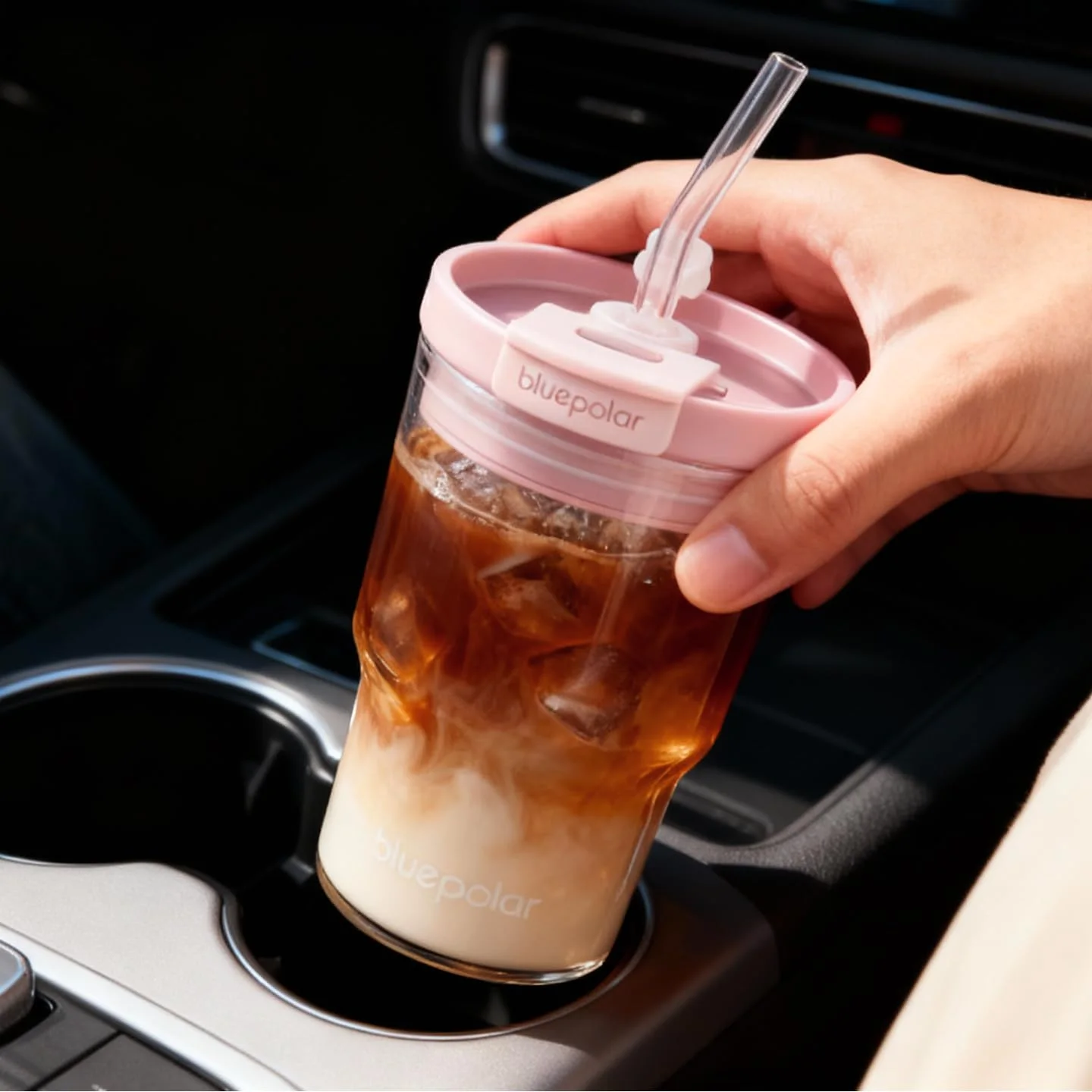 The 16 oz pink-lid glass of iced coffee going into a car cup holder.